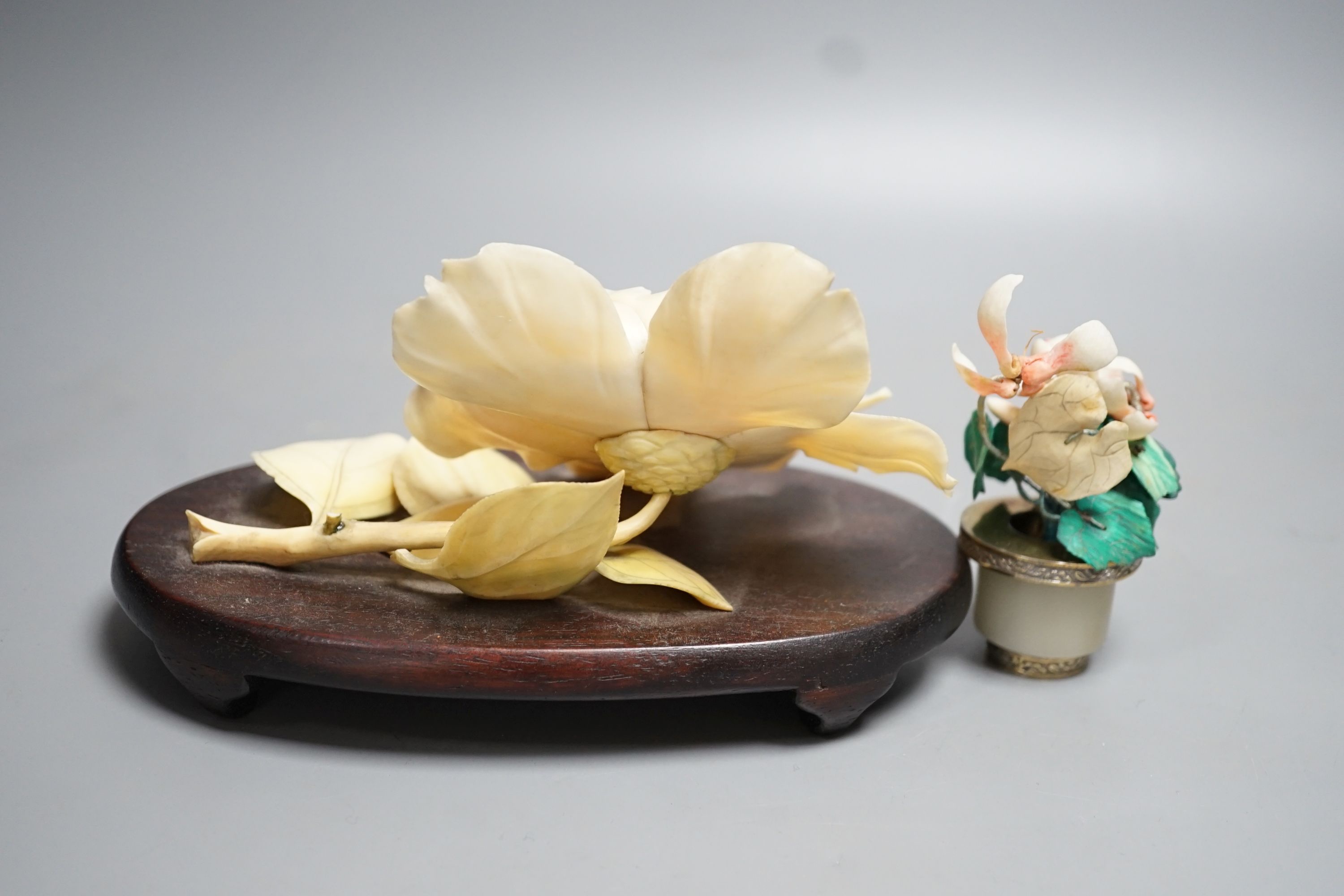 A Chinese ivory model of a peony flower on stand and a Chinese coloured ivory model of flowers with a white jade and white metal plant pot, first half 20th century. Largest measurement 19cm